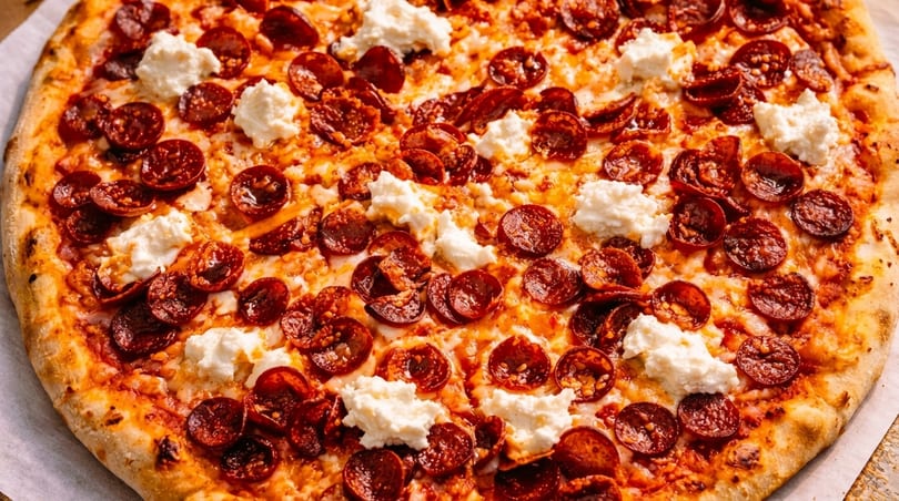 Close-up of a pepperoni pizza with dollops of ricotta cheese and a golden-brown crust.