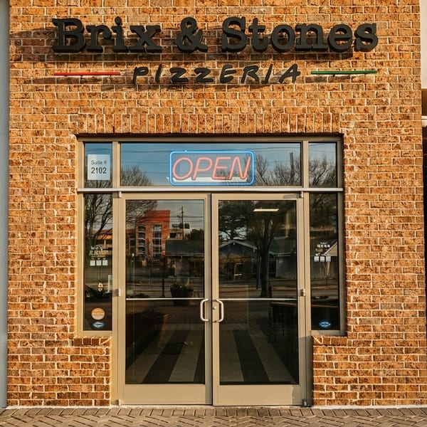 Exterior of Brix & Stones Pizzeria with a brick facade, glass doors, and an "OPEN" neon sign.